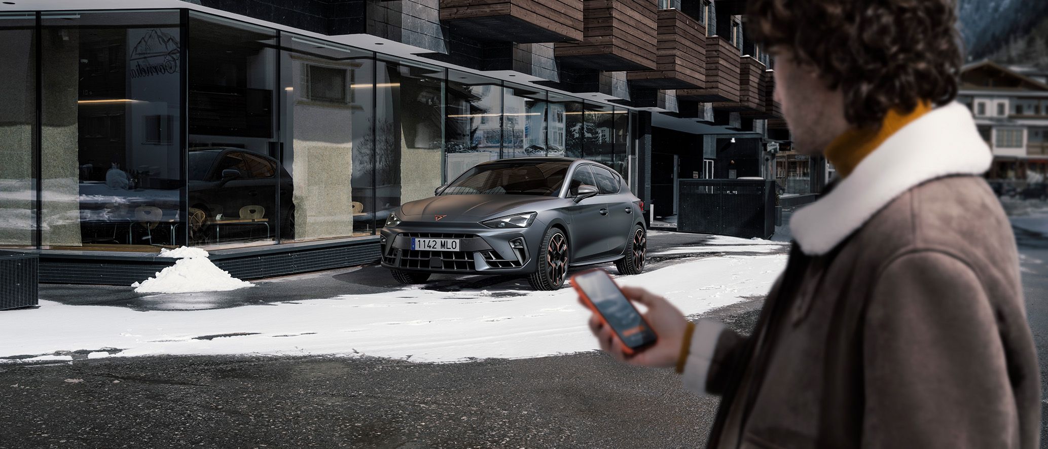 Man met telefoon in de hand naast een CUPRA Leon in de sneeuw